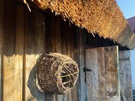 Rustic wooden building with thatched roof and handwoven wicker basket on wall photo