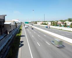 busy highway with vehicles in motion under clear blue sky, showcasing urban infrastructure and greenery photo