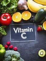 Fresh fruits and vegetables rich in Vitamin C, including oranges, strawberries, and broccoli, arranged around chalkboard photo