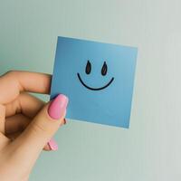 hand holding blue sticky note with smiling face emoji, conveying positivity and joy photo