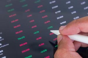 Businessman holding a pen pointing to stock market financial data interface on digital screen photo