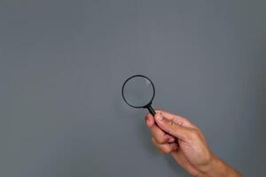 Man's hand holding a magnifying glass with copy space on a gray background photo
