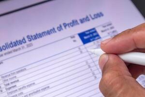 An auditor analyzing Profit and Loss report data. Hand holding a pen and reviewing financial data on digital screen. photo