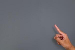 A man's hand with a pose or gesture pointing with index finger at something on a gray background photo