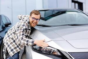 Bearded man embracing his new car at the dealership smiling joyfully photo