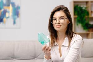 Woman holding a mask nebulizer inhaling fumes medication into lungs. Caucasian sick lady inhaling through inhaler mask at home. Self treatment of the respiratory tract using inhalation nebulizer photo
