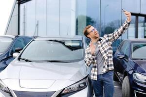 Happy man taking selfie through smart phone after purchasing new car. The man showing the purchased car via link over the phone. photo