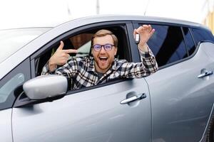Young man showing a car key, sitting inside his new vehicle photo