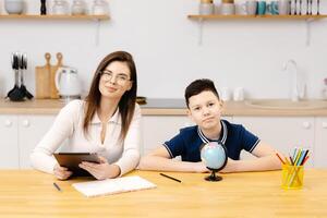 A young woman helps a boy with his lessons using a tablet and a globe. A homeschooling student does his homework with the help of a tutor. photo