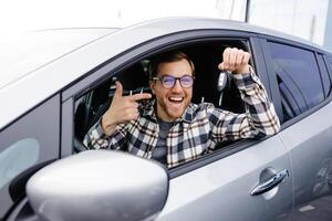 Excited man showing a car key, sitting inside his new vehicle. photo