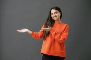Brunette woman standing over blue background with a big smile on face, pointing with hand finger to the side looking at the camera. photo