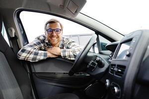 Man looking through window inside new car, checking it before purchase at modern dealership store. Cheerful guy buying or renting automobile at showroom. photo