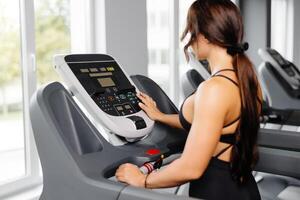 Young sports woman is working out in gym, she doing cardio training on treadmill. Running on treadmill. photo
