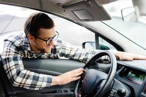 Young man looking through window inside new car, checking it before purchase at modern dealership store. Guy buying or renting automobile at showroom. photo