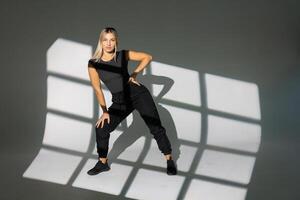 Dancer posing in studio with window light shadows, wearing black clothes. photo