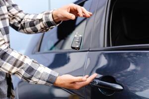 Guy holding key in hand and smiling at camera. Man showing key from his new electric car. Young man buying auto at dealership salon photo