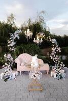 Elegant chaise lounge under floral arch with chandeliers for outdoor wedding ceremony photo