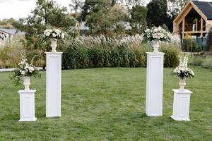 Wedding ceremony setup featuring white columns, flower arrangements, and chairs on a green lawn photo