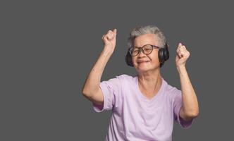 Senior Asian woman wearing wireless headphones with a smile while standing on a gray background photo