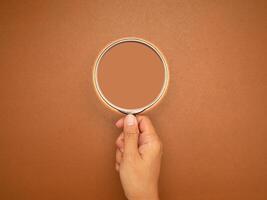 Magnifier in hand with a brown background photo