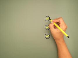 Hand holding a pen check-marking on the checklist box on a green background. Top view. photo