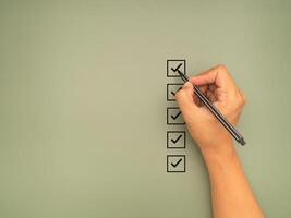 Hand holding a pen check-marking on the checklist box on a green background photo