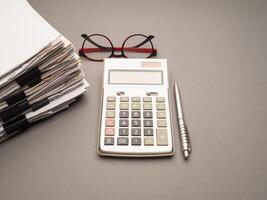 Stack of documents with binder clips, glasses, and calculator on a table photo