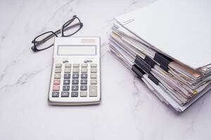Stack of documents with binder clips, calculator on a marble table photo
