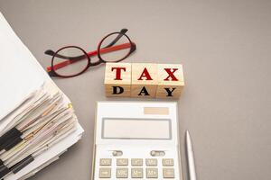 Stack of documents with binder clips, glasses, calculator, and Wooden cubes with the letters TAX on a gray background. Top view. photo