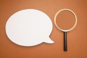 Top view of a blank white speech bubble and a magnifying glass isolated on a brown background photo