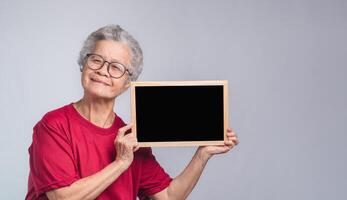 Senior woman holding a mini blackboard and looking at the camera with a smile while standing on a gray background. photo