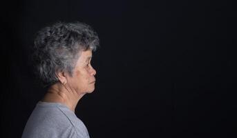 Side view of a senior woman looking away with a smile while standing on a black background photo