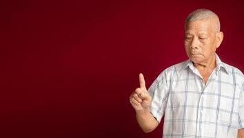 Senior man in a white shirt showing a finger with a smile while standing on a red background photo