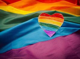 Top view of a rainbow heart shape symbol made from paper over the rainbow flag or LGBT flag. photo