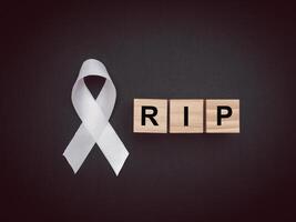 Top view of a white ribbon and wooden cubes with the letters RIP on a black background photo