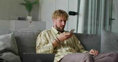 A man sitting on a couch with a laptop and cell phone video