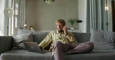 A man sitting on a couch with a laptop and talking on the phone video