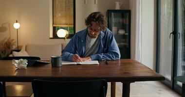 A man sitting at a table writing in a notebook video