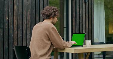A man sitting at a table with a laptop and green screen video