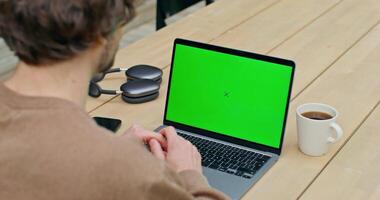 A man is sitting at a table with a laptop and a green screen video