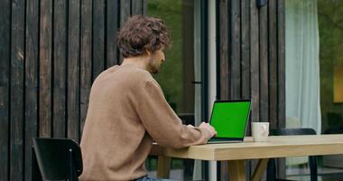 A man sitting at a table with a laptop and green screen video