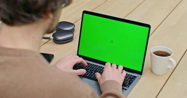 Man typing on laptop with green screen video