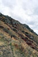 Group of hikers trekking along a rocky hillside under a cloudy sky in a mountainous region during autumn photo
