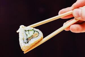 Hand holding sushi roll with chopsticks against dark background in a minimalist setting photo