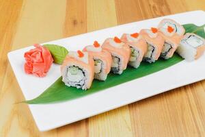 Fresh sushi rolls featuring salmon, cucumber, and a decorative rose on a white platter with a green leaf photo