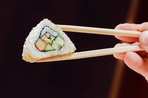 Sushi roll held with chopsticks showcases fresh ingredients and meticulous preparation in a modern setting photo