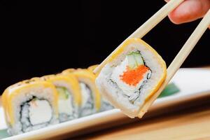 Sushi roll with cream cheese and fish roe being held by chopsticks at a restaurant table during dinner time photo