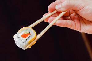 Hand holding sushi roll with chopsticks against dark background in a culinary setting photo