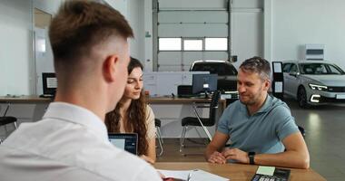 A man and woman are talking to a man in a car dealership video