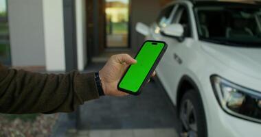 A man is holding a smartphone with a green screen in front of a car video